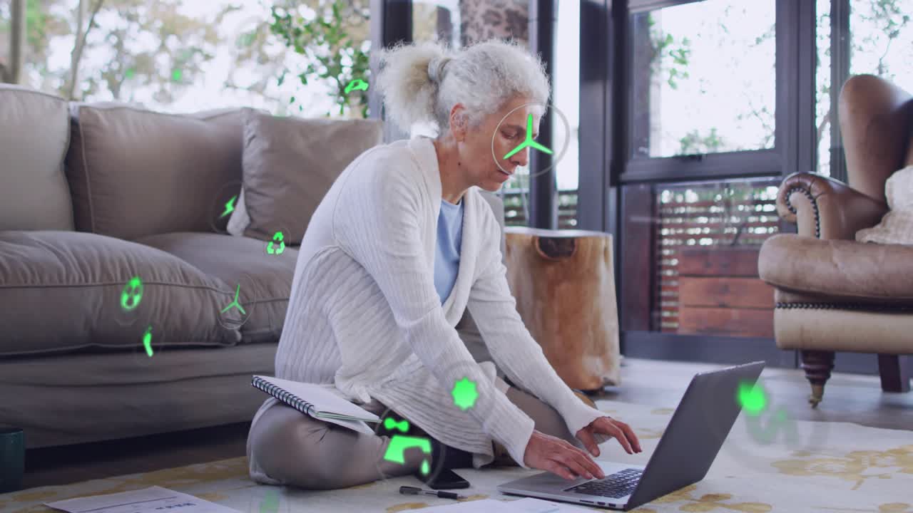 Woman writing notes reaching phone shifting to laptop doing energy plan with green icons overlaying