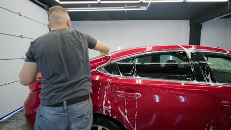 man worker washing red car on a car wash with yellow washcloth.