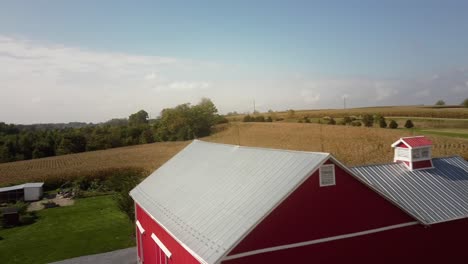 Aerial-of-a-red-farmhouse-in-Pennsylvania-rural-area,-surrounded-by-cornfield-and-trees