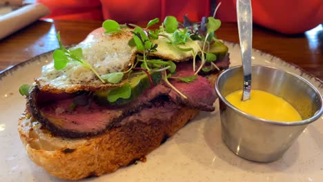 sabroso sándwich de carne asada de pastrami con pepinillos, huevo frito, microgreens y mostaza, tostadas para el desayuno, almuerzo en un restaurante, tiro de 4k