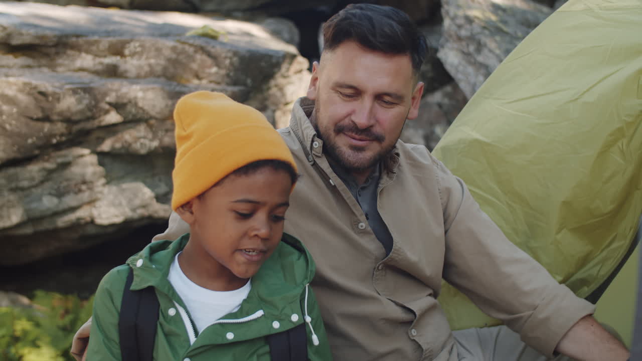 un niño de raza mixta hablando con su padre en el campamento.