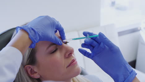 woman sitting in chair being give botox injection between eyes by female doctor