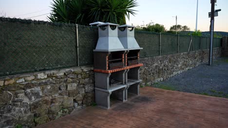 outdoor stone grill setup against a fence in a rustic setting at dusk. static