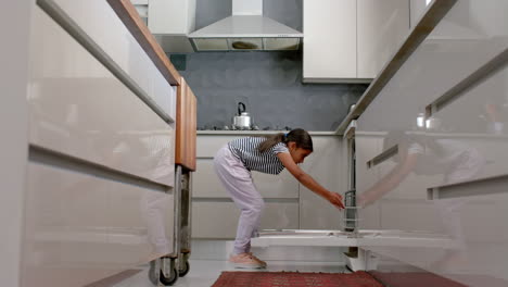 happy biracial girl loading dishwasher in kitchen, copy space, slow motion