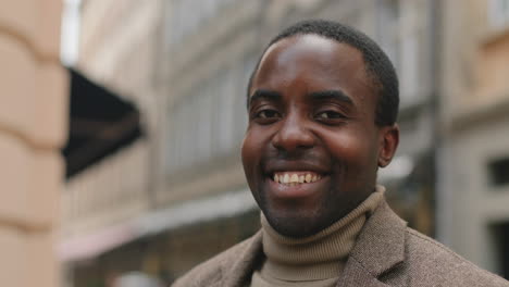 close-up view of african american cheerful businessman with beard in elegant clothes looking at the camera and smiling on the street