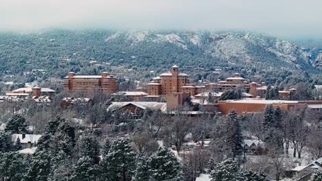 Dusting-of-snow-sits-on-conifer-and-deciduous-trees-at-base-of-Rocky-Mountains-with-destination-luxury-hotel-at-center