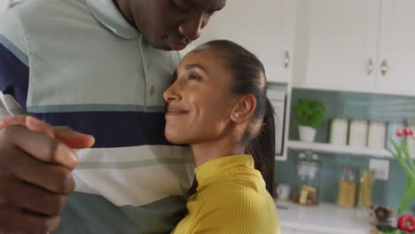 Video-of-happy-diverse-couple-slow-dancing-together-and-smiling-in-kitchen