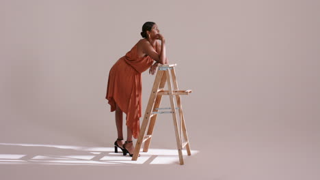 sunlight grid drawing indian woman into studio and posing in orange dress on ladder, copy space