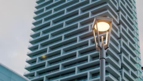 Moderne-Straßenlaterne-Vor-Einem-Futuristischen-Hochhaus-Mit-Eigentumswohnungen-In-Der-Abenddämmerung