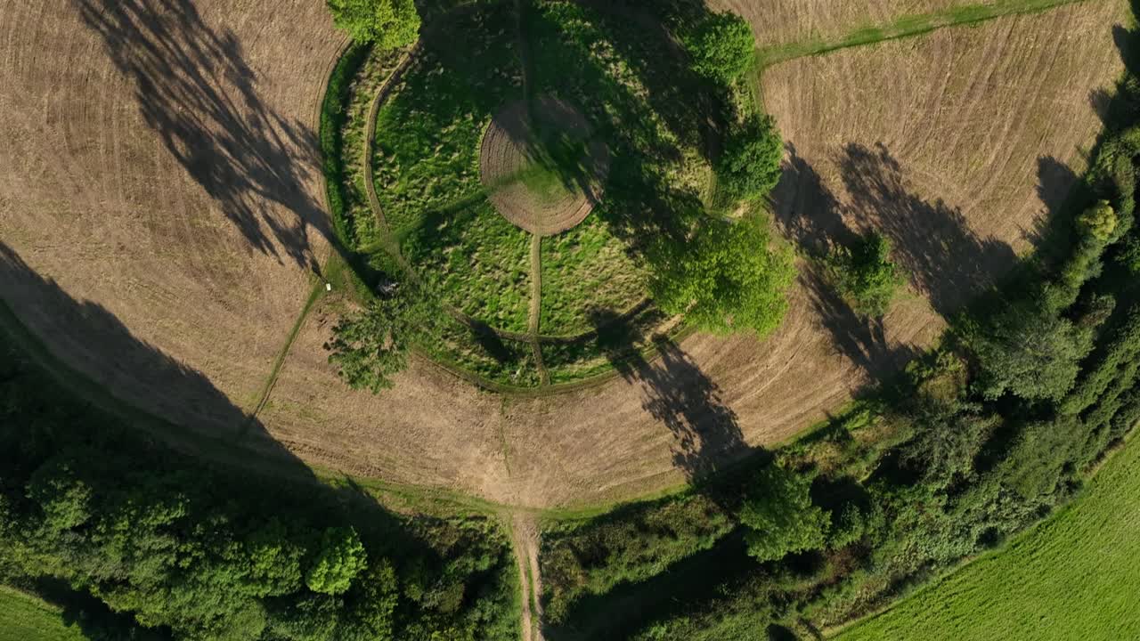 The Navan Fort, County Armagh, Northern Ireland, September 2022. Drone top down bird's eye view pan across top of circular hilltop with cultural heritage site and winding trails down hillside.