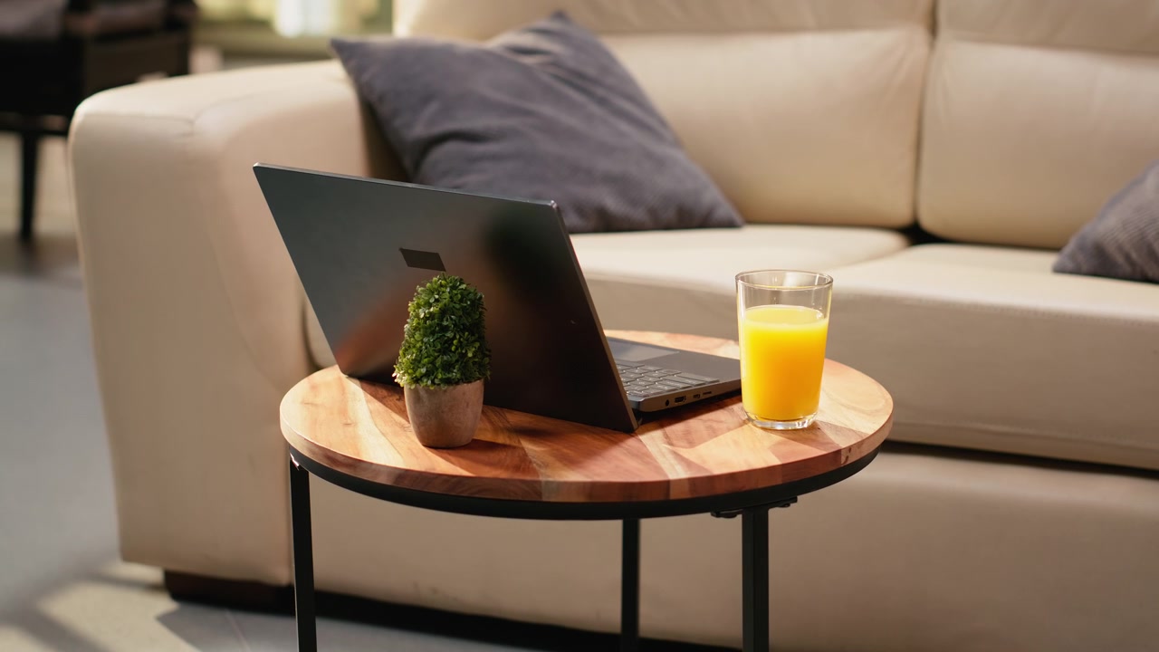 Laptop and orange juice glass placed on wooden coffee table