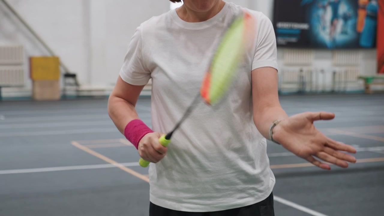 Donna che pratica badminton. Si prepara per la partita attraverso una gestione precisa dell'attrezzatura e la concentrazione. Ambiente sportivo interno dove la donna affina racchetta e volano per prestazioni ottimali.