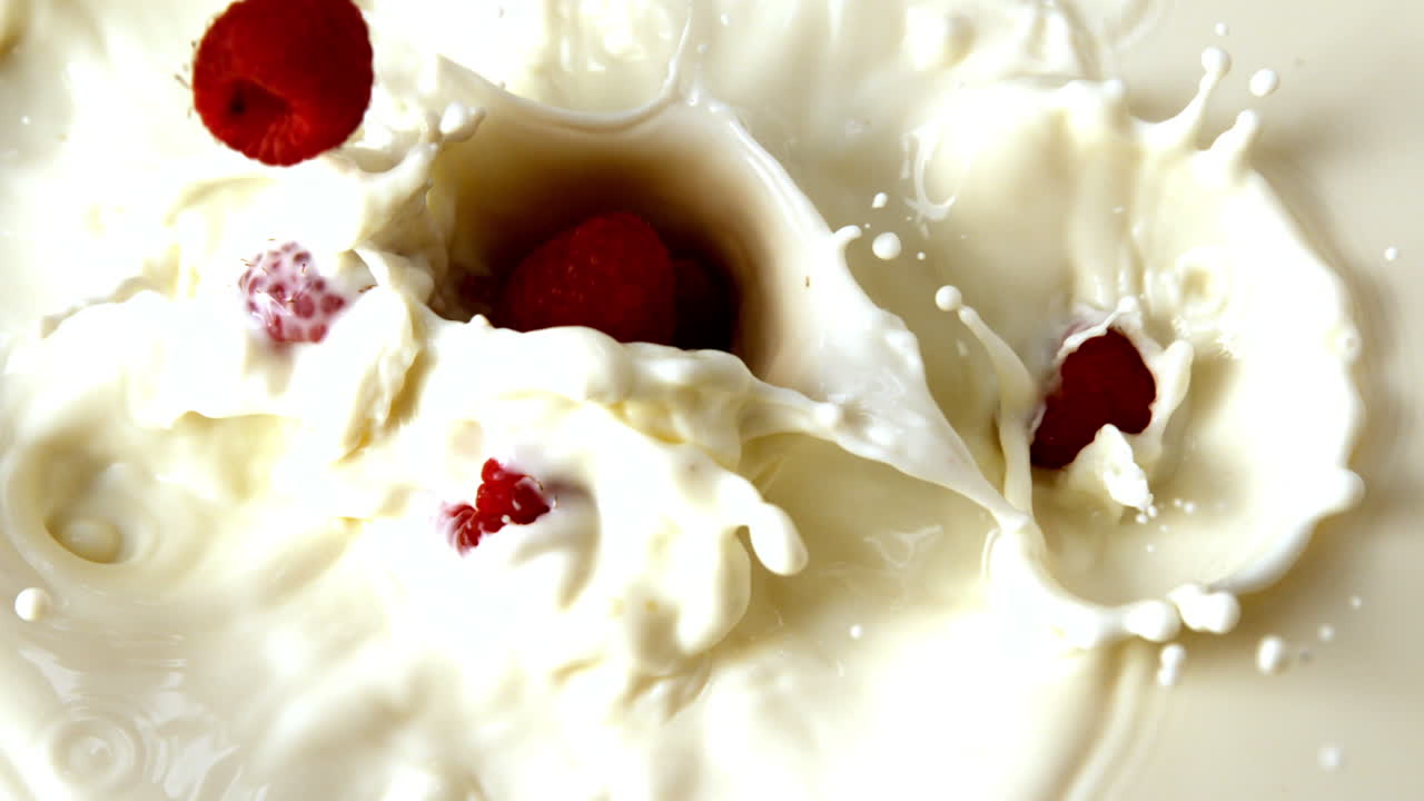 frambuesas que caen en un vaso de leche