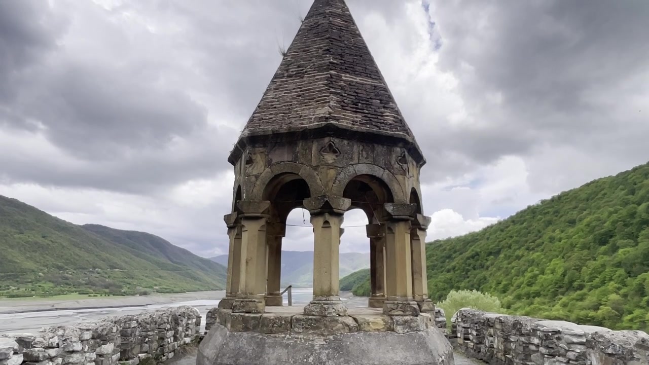 Ripresa dal basso con inclinazione verso l'alto di un'antica torre campanaria in pietra presso la Fortezza di Ananuri, che si affaccia sul fiume Aragvi, Georgia.