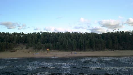 Gente-Haciendo-Parapente-En-La-Playa-Con-Bosque-Al-Fondo