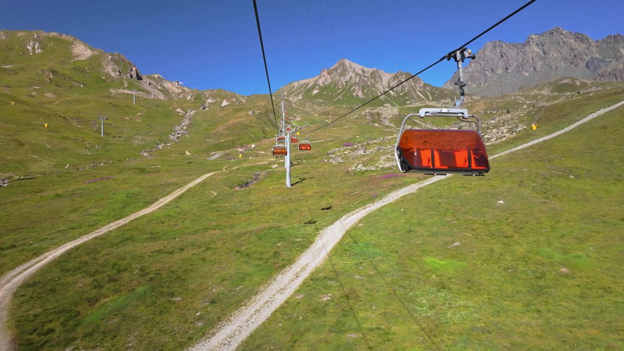 Seggiovia Flimsattelbahn a Samnaun che porta al punto panoramico per selfie di Ischgl, al confine tra Austria e Svizzera, con cime, pendii verdi, sentieri e un cielo azzurro limpido in estate.