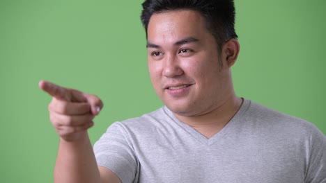 young handsome overweight asian man against green background