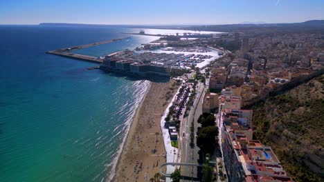 aerial drone shot of playa del postiguet in alicante spain with the marina and small sailing ships in the background