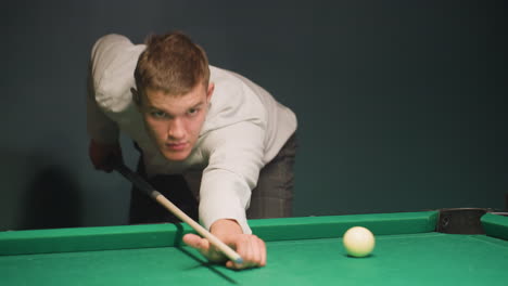 close-up of gentleman in white shirt leaning over green pool table, gripping cue stick with intense focus. he takes a shot as the ball rolls back, demonstrating precision, concentration