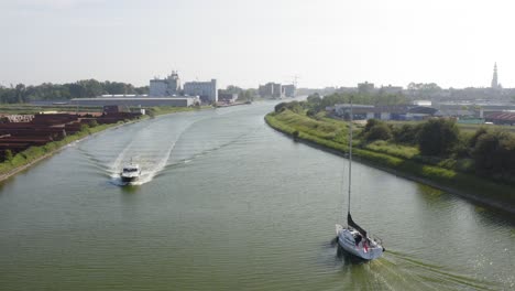 Tracking-shot-of-a-sailboat-passing-another-boat-on-the-Canal-through-Walcheren-in-Zeeland,-the-Netherlands,-on-a-sunny-summer-evening