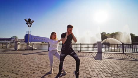 street dance. young couple of professional dancers on the background of beautiful fountain outdoors. boy in black and girl in white performing freestyle dance.