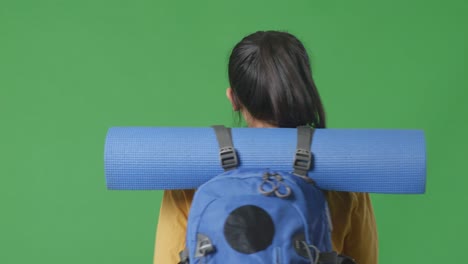 close up back view of a female hiker with mountaineering backpack looking around while walking on green screen background in the studio