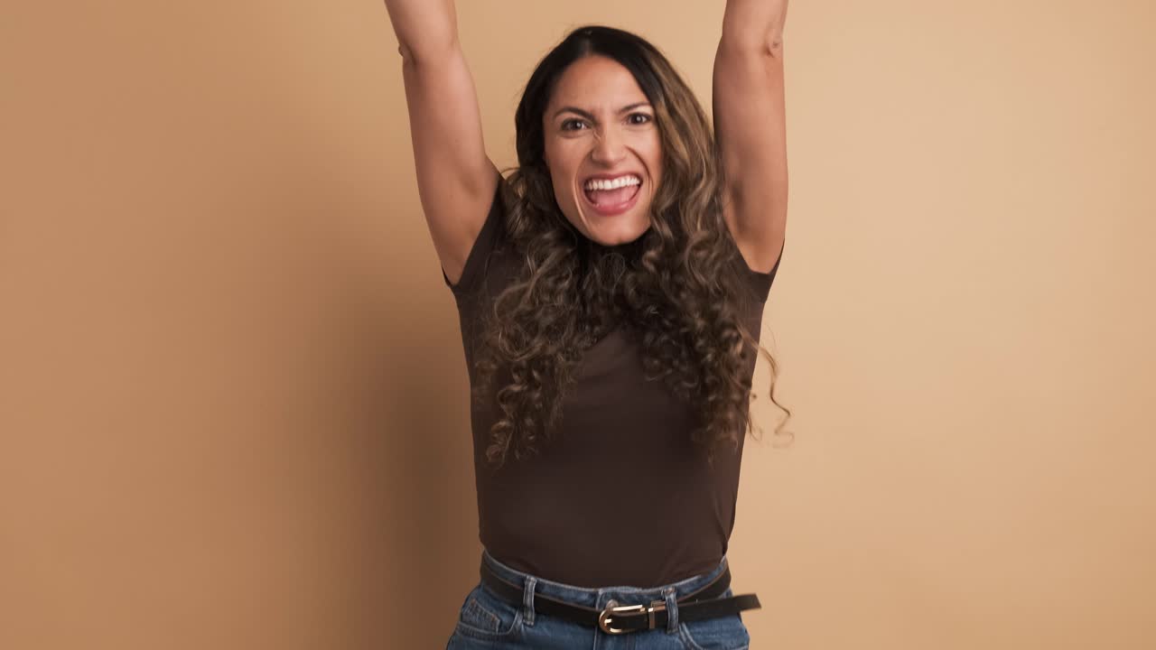 Happy hispanic woman celebrating raising fists and looking at camera