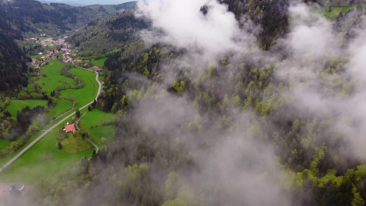 Drone slow fly over a forest mountain valley with a rural road through moody clouds during spring time