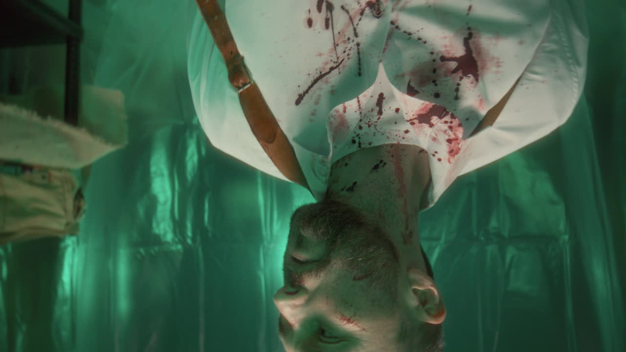 una toma de un hombre atado con una camisa manchada de sangre tratando de escapar de una trampa.