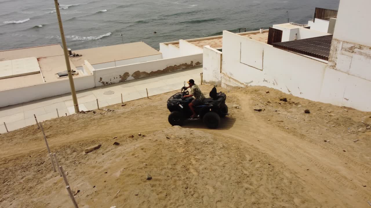 Ripresa aerea di una persona che guida un ATV o un quad su un sentiero sterrato in una località di mare