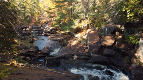 river streaming through hilly rocky terrain of autumn forest, dolly forward