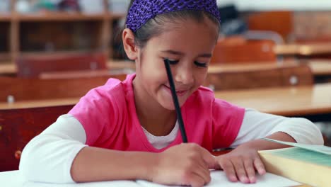 cute little girl colouring in book in classroom smiling at camera