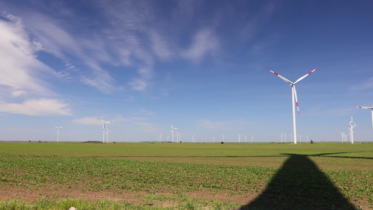 Long shadow under windmill, large wind power turbines spinning to generating clean, green, renewable energy