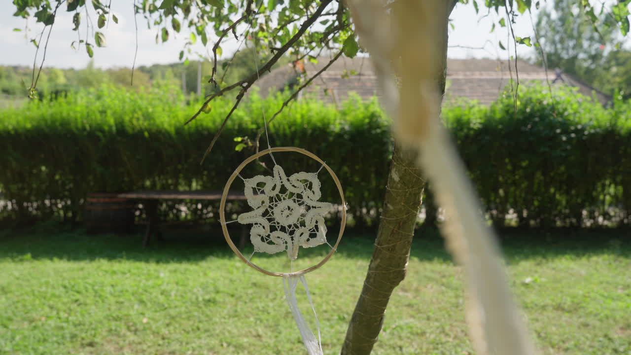 A beautiful white dream catcher swaying gently in the wind on a farm, adding a touch of serenity and boho charm to the rustic countryside setting.