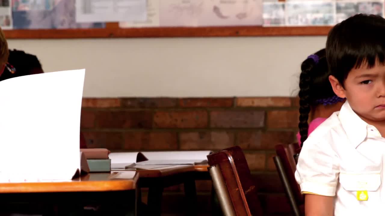 슬픈 작은 소년이 수업 중에 카메라를 보고 있습니다.