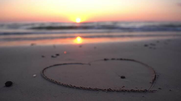 Hart symbool getekend in het zand tegen een achtergrond van zonsondergang boven de zee