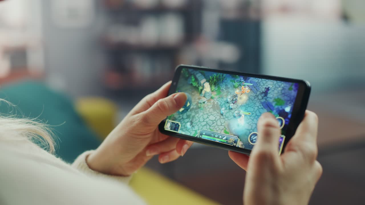cerca de las manos jugando un videojuego de estrategia rpg en un teléfono inteligente sostenido horizontalmente en la sala de estar de la casa. manos femeninas tocando la pantalla del teléfono móvil con un juego colorido a través de internet.