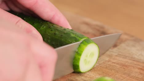 Cutting a cucumber with a knife on a cutting board.