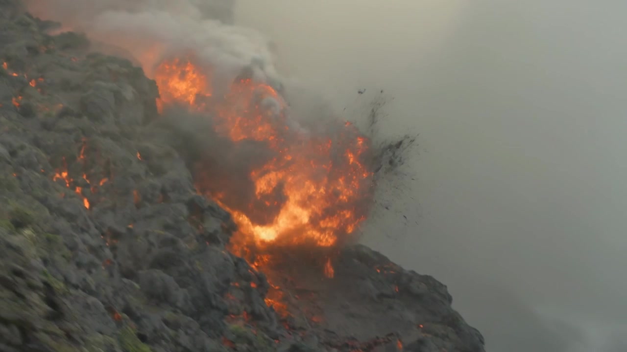Accensione di focolai incandescenti su ripido pendio roccioso, fiamme che si muovono nelle fessure sprigionando braci, spazio per il testo.