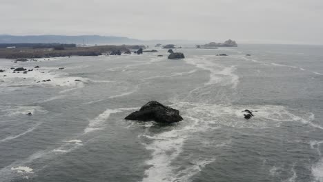 stormy day aerial of a rocky ocean shore, flying toward a dark rock in the ocean, waves crash against dark sea rocks, the sky looks dark with clouds