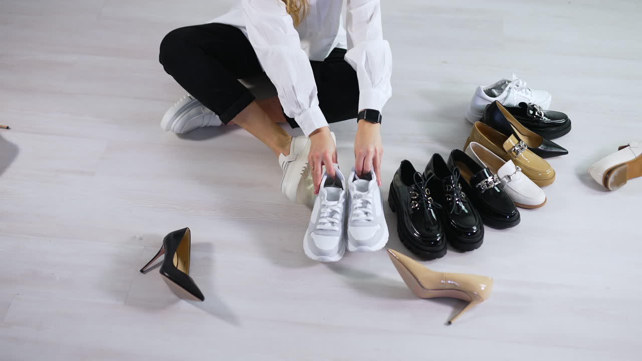 Lady on the floor puts different shoes in pairs in front of hers. Demonstrating the diversity of female footwear. White backdrop.