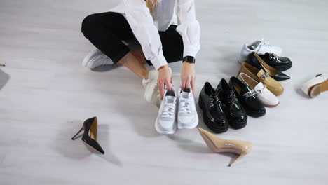 lady on the floor puts different shoes in pairs in front of hers. demonstrating the diversity of female footwear. white backdrop.