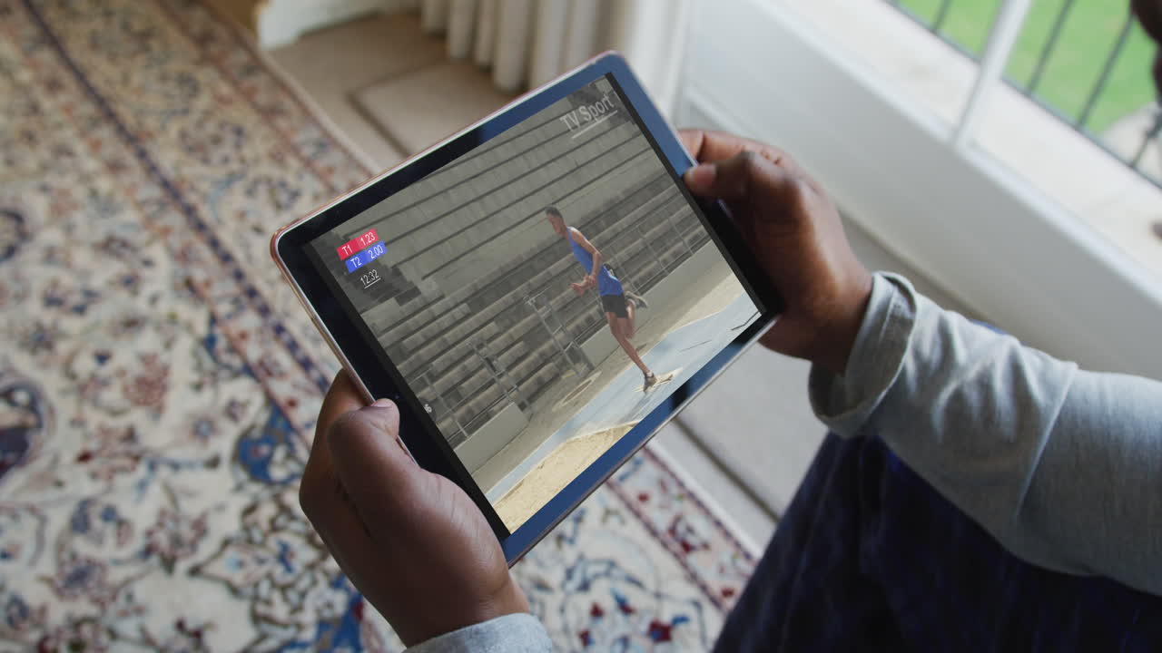 Composite of man sitting at home watching athletics long jump event on tablet
