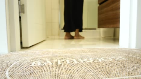 a person standing on a bathroom rug with the word "bathroom" on it.