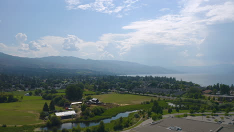 Vista-Aérea-De-La-Comunidad-Suburbana-De-Kelowna-En-Un-Día-Soleado,-Cerca-Del-Lago-Okanagan,-Con-Montañas-Distantes-Visibles-En-La-Neblina