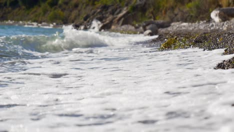 las olas espumosas del mar jónico bañan las rocas de la playa