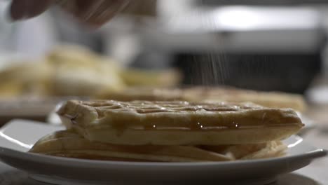 sprinkling cinnamon on top of freshly cooked waffles in plate - close up, selective focus