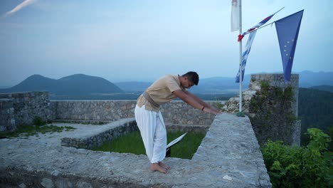 imagen panorámica de un hombre indio adulto en almidón antes de hacer hatha yoga descalzo con ropa tradicional de yogui en la cima de la colina en la pared del castillo al amanecer