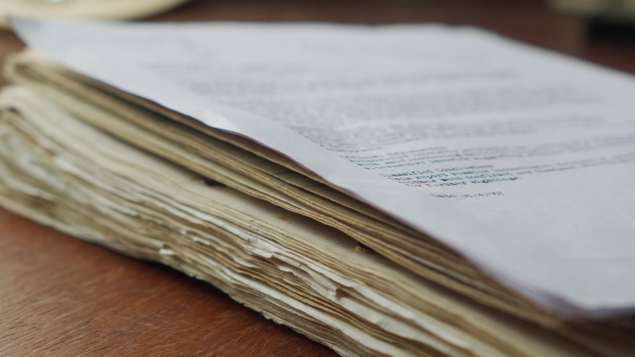 Close-up side view of aged documents landing on a pile, suggesting case files, research buildup, or uncovering hidden archive information.
