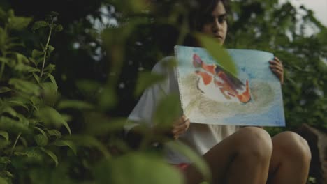 slow reveling shot of a young teenager holding a painting of fish with a concept of conservation of the ecosystem